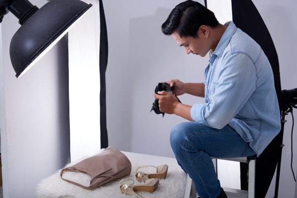 Young Vietnamese man taking photos of fashion items in studio
